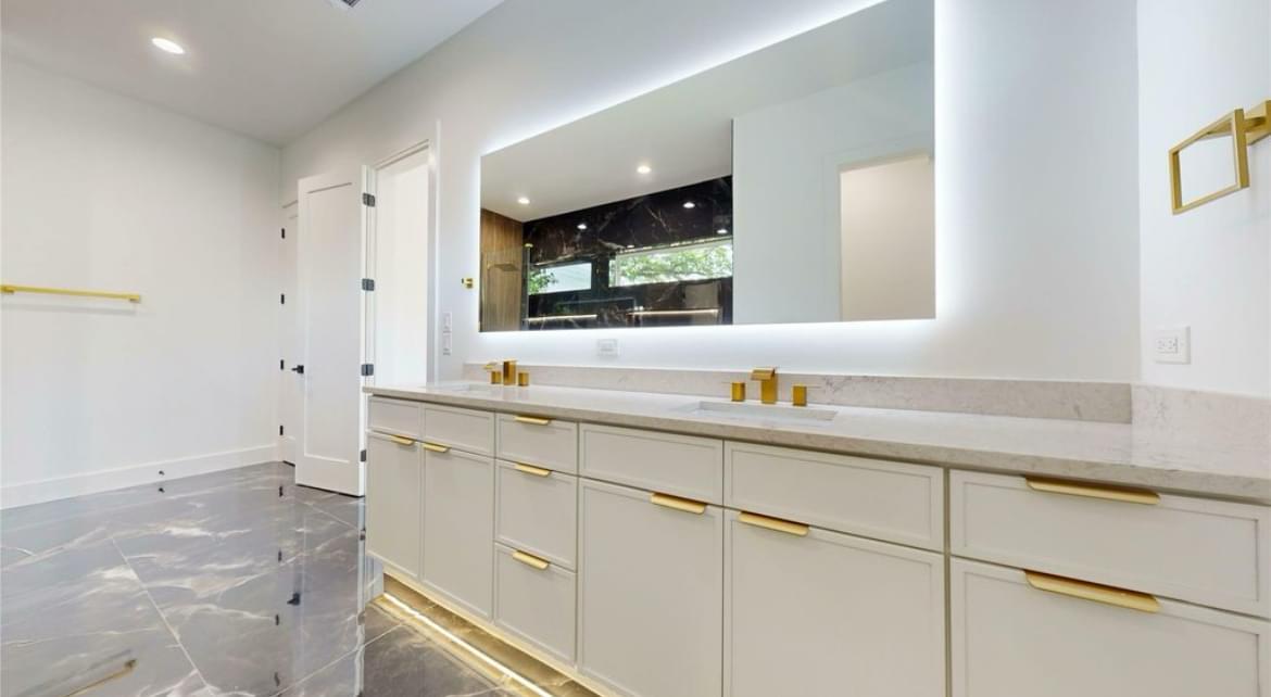 Bathroom remodel with large backlit mirror, gold fixtures, and sleek cabinets